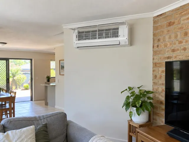 Clean split system indoor unit on a living room wall above a plant and TV in Ormeau